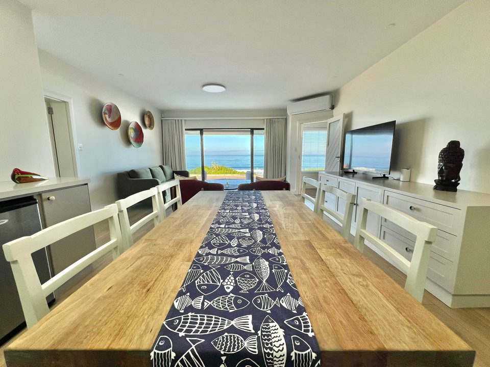 De lange tafel in de benedenwoning, met de zee achter de glazen deuren