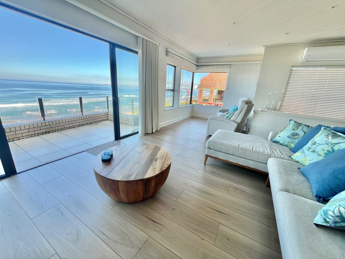 Das Wohnzimmer im Obergeschoss mit dem Ozean hinter der Glasfront, die Türen zum Balkon geöffnet